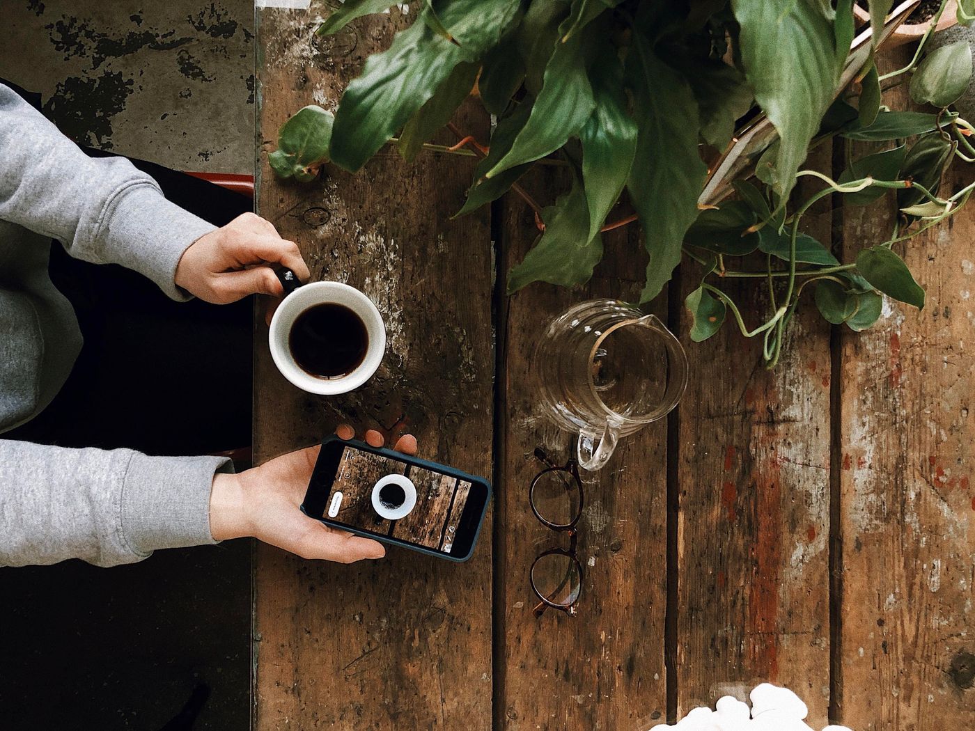 A person holding a phone and a coffee at a wooden table